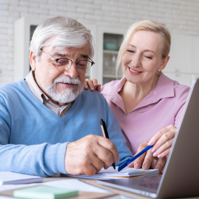 Close up image of a senior couple searching on a laptop and writing on a notebook