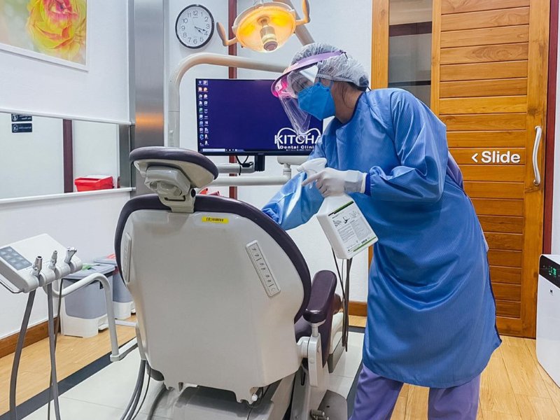 A dental chair and room surfaces being wiped with a disinfectant solution to kill viruses and bacteria, ensuring a clean and safe environment.