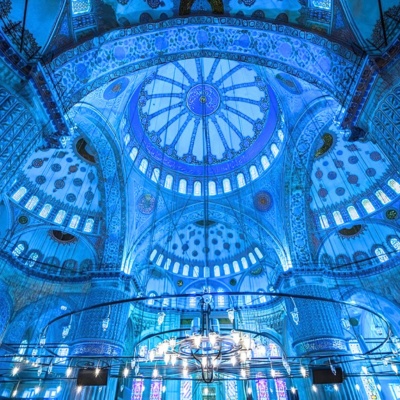 Inside view of the Blue Mosque’s dome, illuminated with soft blue lights, showcasing intricate Islamic architecture and patterns