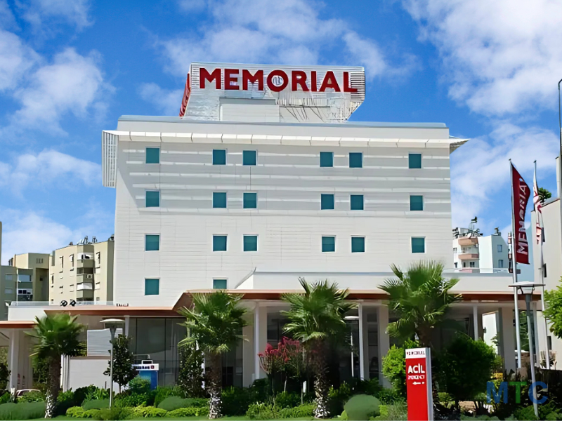 Exterior view of Memorial Hospital Antalya, featuring a white building with lush green landscaping in front.